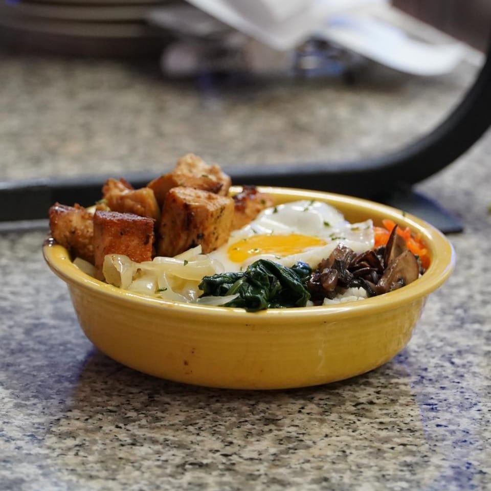 An Asian-fusion bowl with fried tofu, egg, spinach, mushrooms, and onions in a yellow bowl.